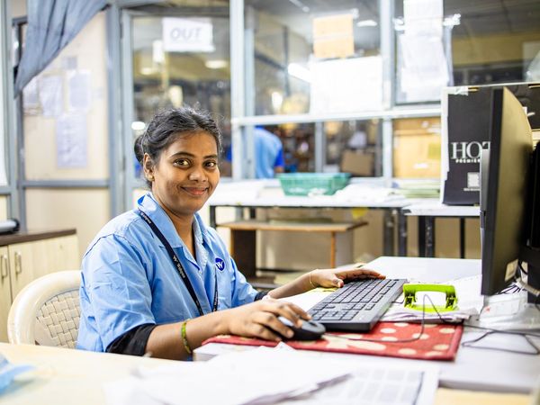 A woman in a work uniform at a desk, working at a computer.