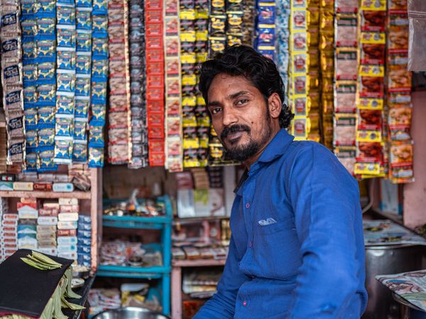 A shopkeeper sitting in his stocked neighbourhood store.